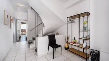 Un interior moderno con una escalera, una silla negra, un estante de madera con objetos y un suelo de baldosas.
