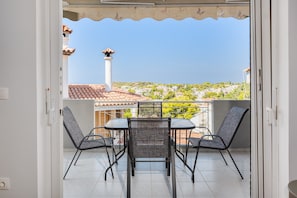 A balcony with a table and chairs, a view of a town, and a tiled floor.