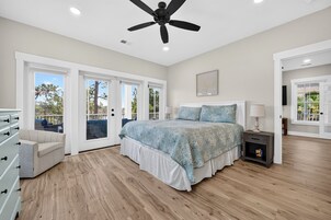 Un dormitorio con una cama, una mesita de noche, un ventilador de techo y vistas a través de puertas de cristal.