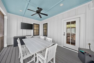 Un patio techado con una mesa de comedor y sillas, un ventilador de techo y un televisor montado en la pared.
