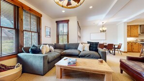 A living room with a sectional sofa, a coffee table, and a dining area with wooden chairs and a table. - Snowcreek Vi The Lodges #1153 2 Bedroom Condo (Mammoth Lakes)