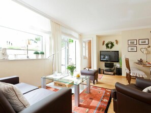 A modern living room with a glass coffee table, leather sofas, a flat-screen TV, and a large window with curtains. - Holiday Apartment in Norderney With Wi-fi (Norderney)