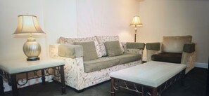 Ein Wohnzimmer mit einer Couch, zwei Lampen, einem Sessel und einem Tisch.