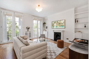 A modern living room with a sofa, a fireplace, and a dining area with a table and chairs. - Spacious Notting Hill 3-bed With a Home Office (London)