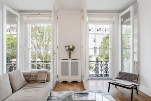 A spacious living room with a sofa, a coffee table, and a chair. There is a radiator in the center and a window with a view of the outside. - Spacious Notting Hill 3-bed With a Home Office (London)