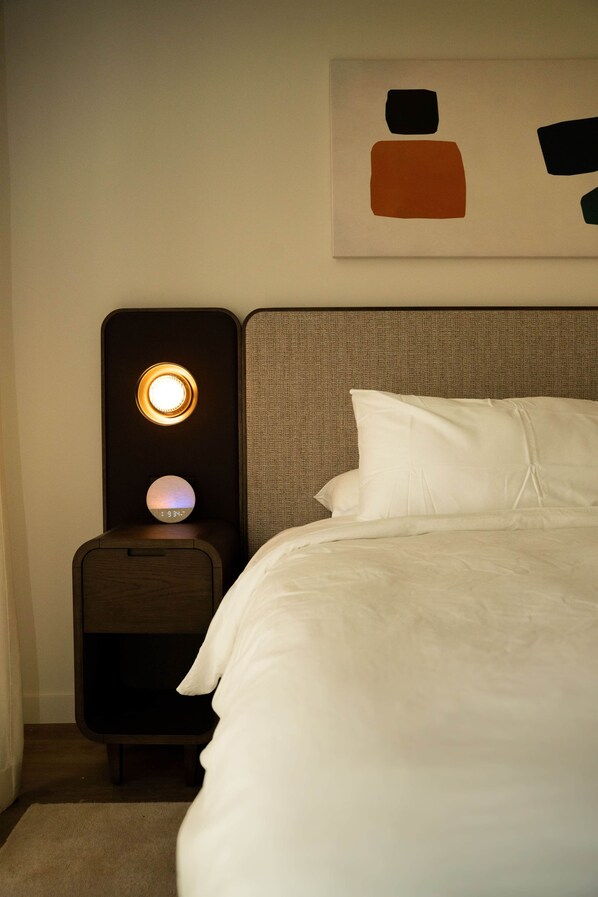 Een hotelkamer met een bed, een nachtkastje met een lamp en een kunstwerk aan de muur.