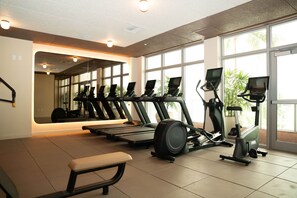 Een sportschool met loopbanden, crosstrainers en een bank.