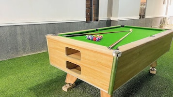 Una mesa de billar con una mesita de madera en una habitación con piso de césped artificial.