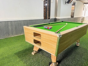 Una mesa de billar con una mesita de madera en una habitación con piso de césped artificial.