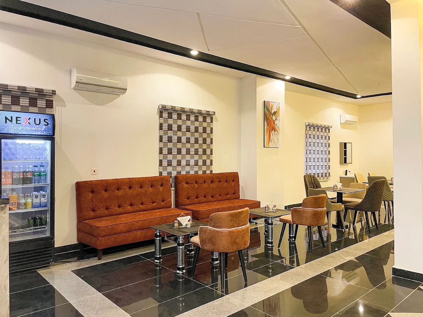 A hotel lobby with a brown sofa, a glass table, and chairs. There is a vending machine labeled 'NEXUS' on the left.