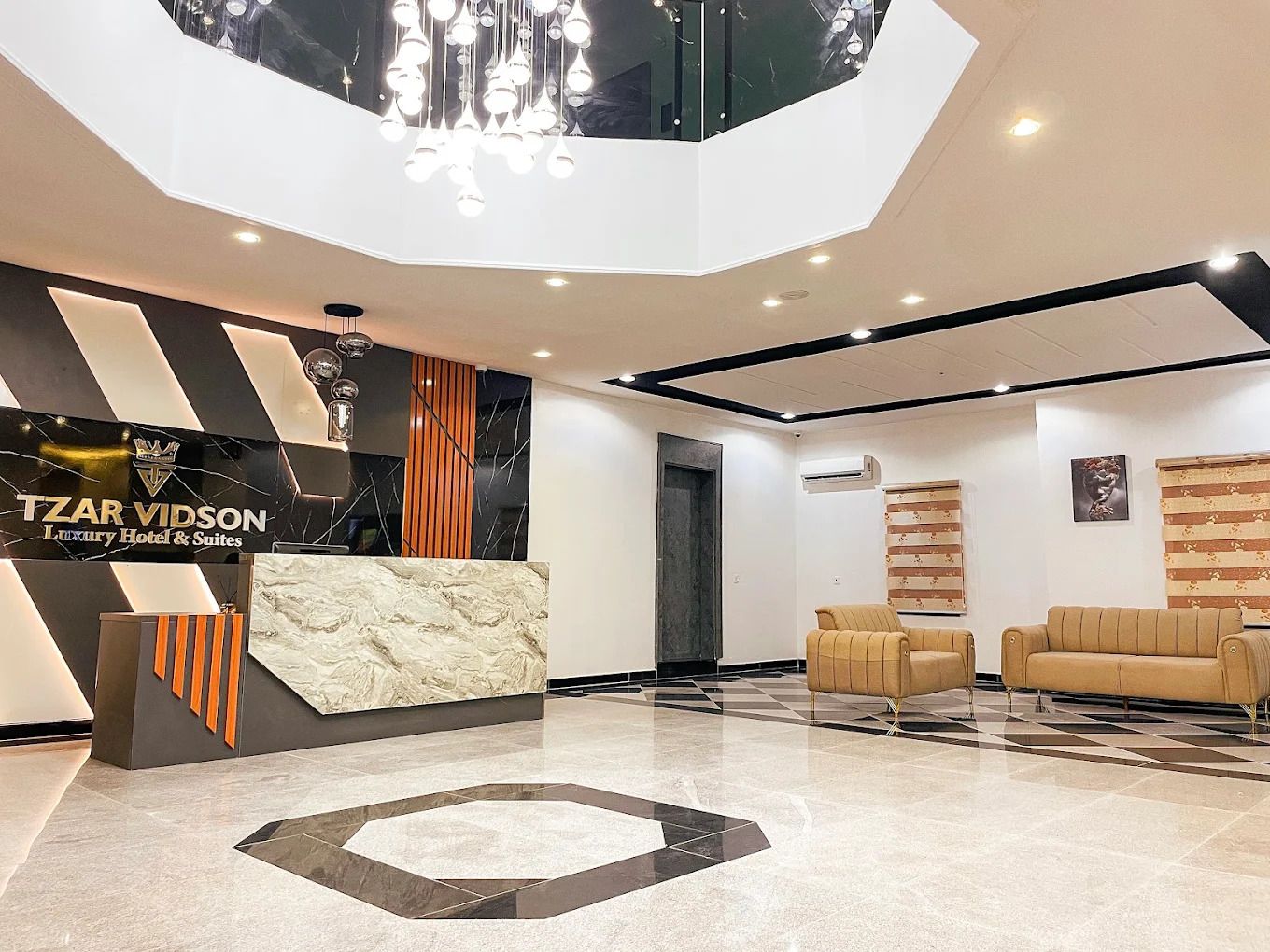 Zona de recepción de hotel con diseño moderno, que incluye un mostrador de recepción, área de estar y un patrón geométrico en el suelo.