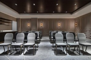 Un salón de conferencias con filas de sillas, un mostrador de recepción e iluminación en la pared.