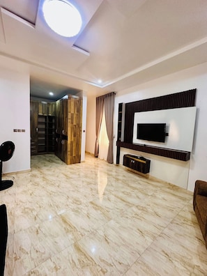 Amplia sala de estar con un televisor de pantalla plana grande montado en la pared, piso de mármol y un diseño de techo moderno.