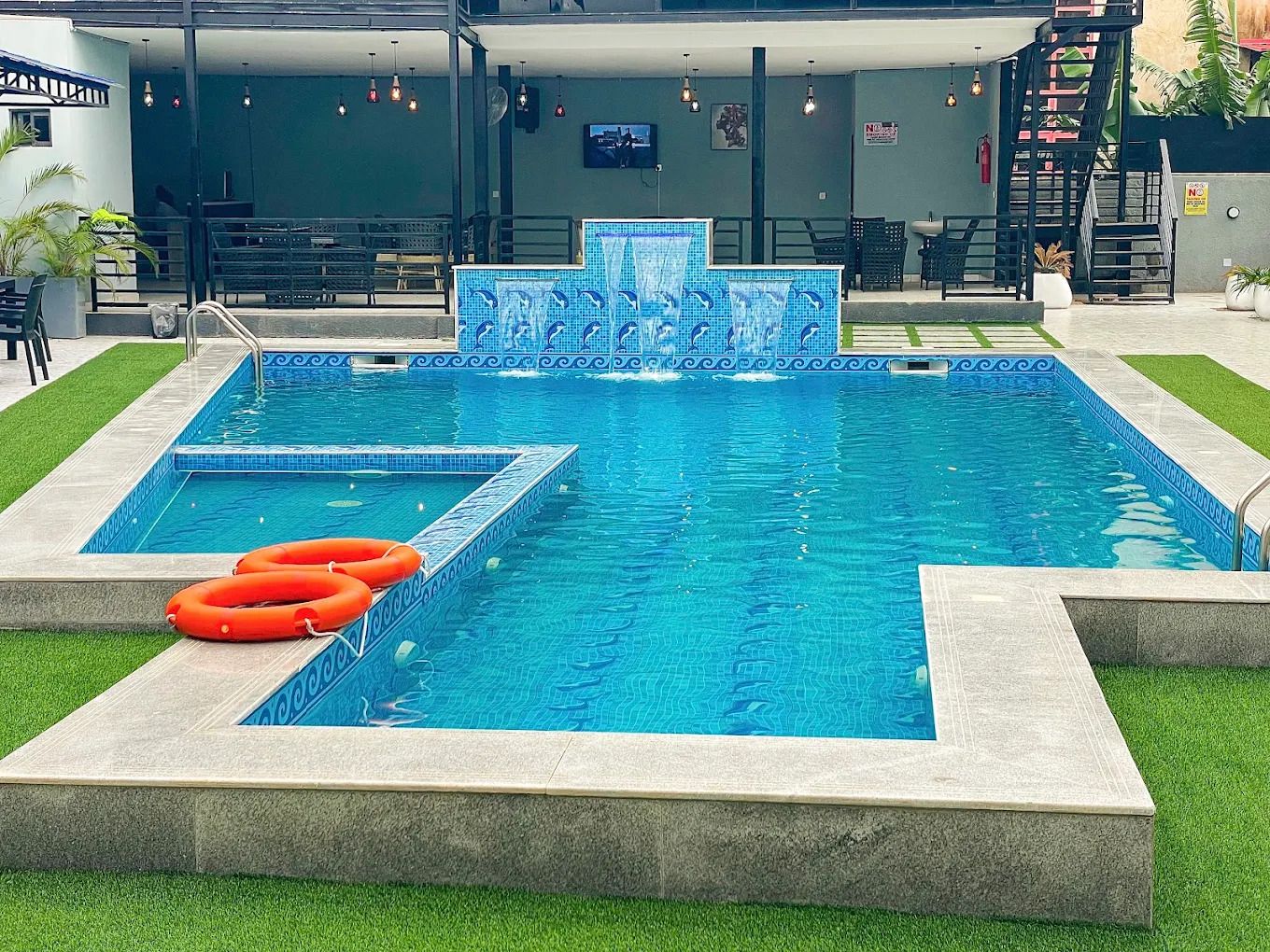 Una piscina con borde de azulejos y una sección separada con un diseño de mosaico diferente. Hay dos flotadores salvavidas en el borde de la piscina.