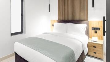 A hotel room with a bed, bedside table, and a window.