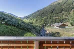 A wooden deck overlooking a mountainous landscape with a house and a stream. - AffittiPontediLegno - Chalet la Mia Baita 2 (Ponte di legno)