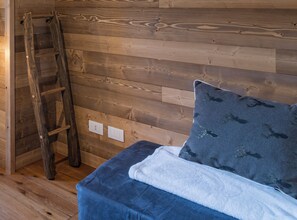 A room with wooden panel walls, a wooden ladder, a bed with a blue and white duvet, and two wall sockets. - AffittiPontediLegno - Chalet la Mia Baita 2 (Ponte di legno)