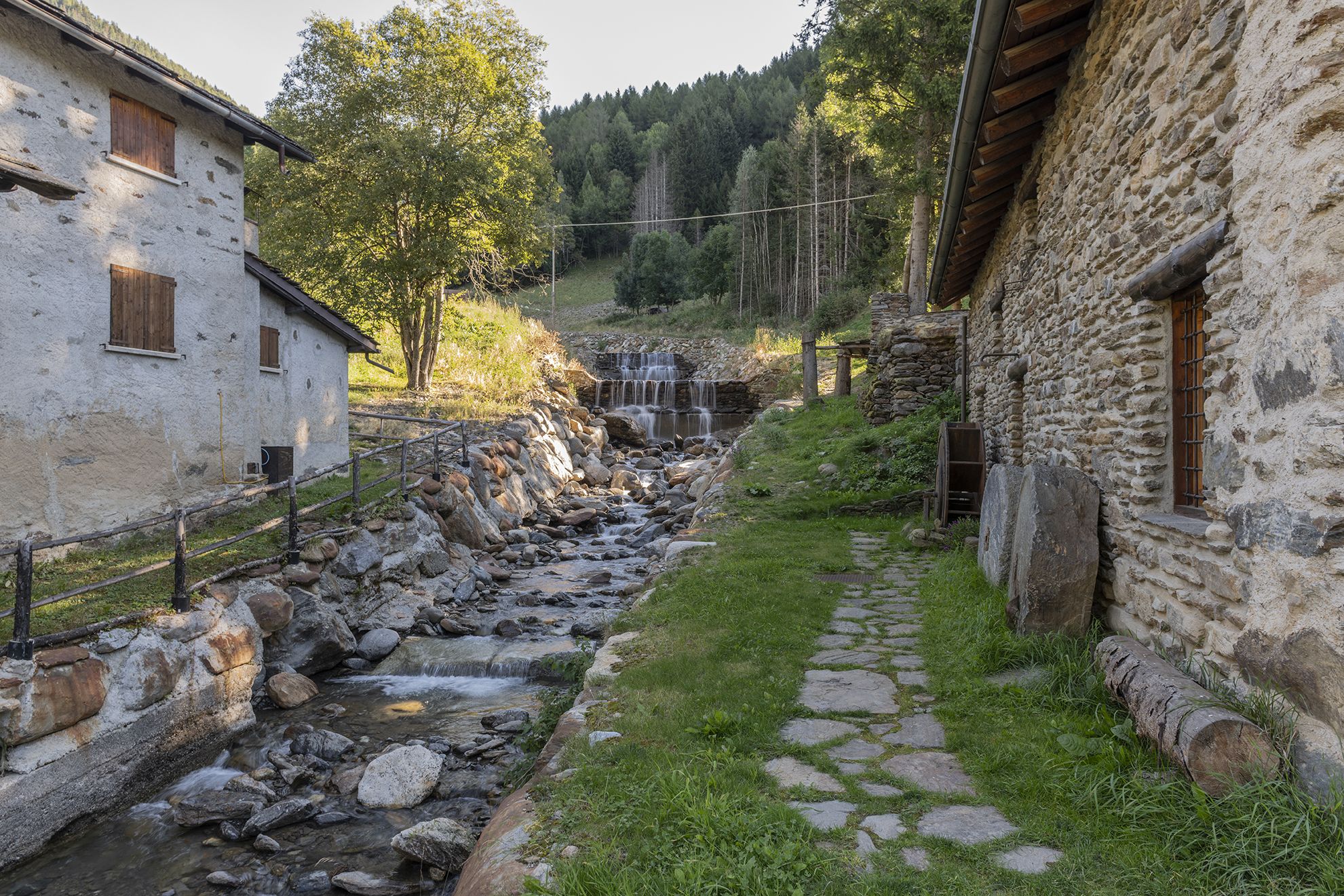 A rustic stone building with a stone pathway leading to a small waterfall.