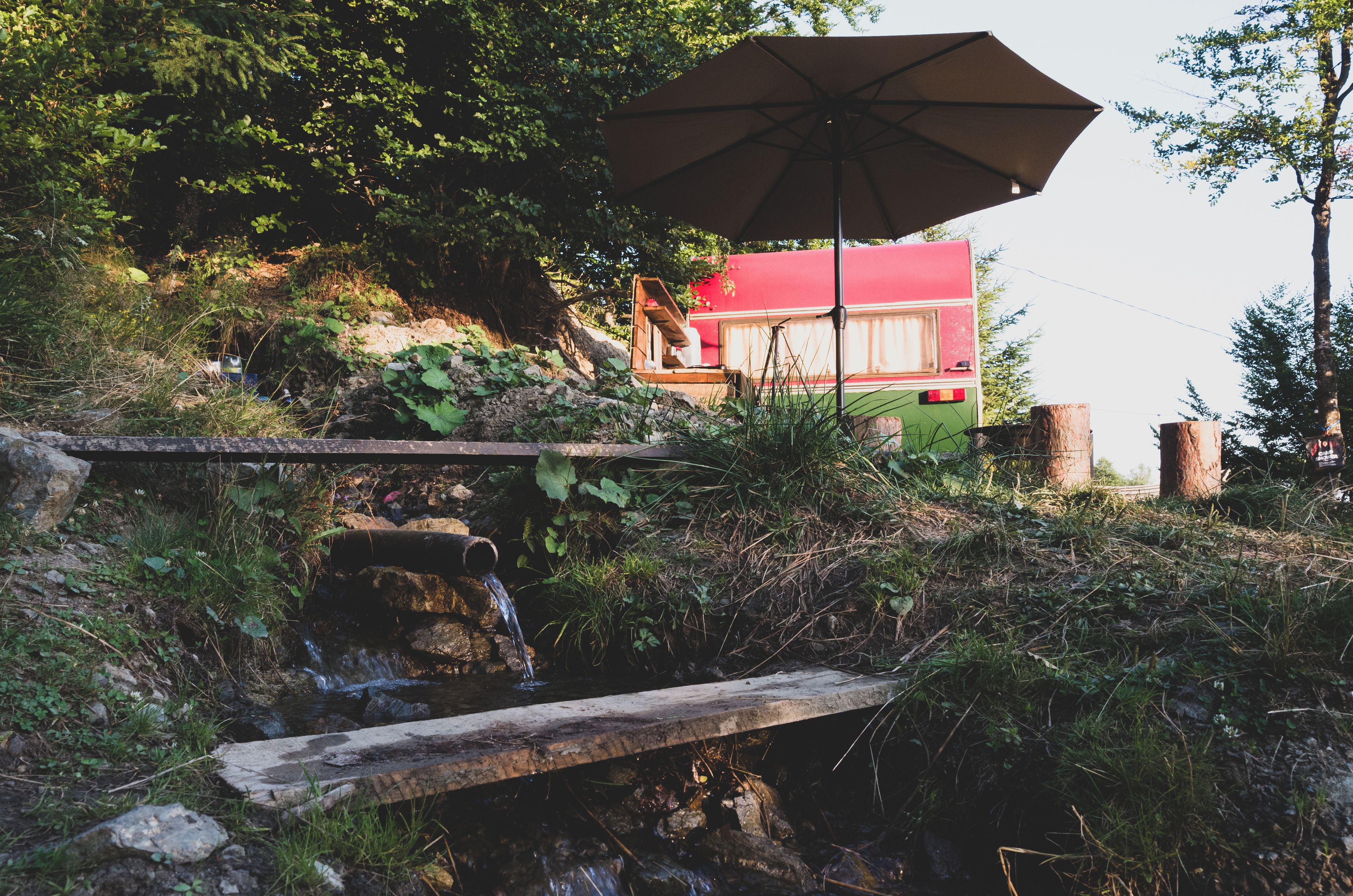 A rustic outdoor setting with a wooden bench, a small stream, and a red house partially obscured by foliage.