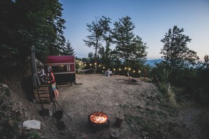 Un camping al aire libre con una fogata, zona de comedor y luces colgantes.