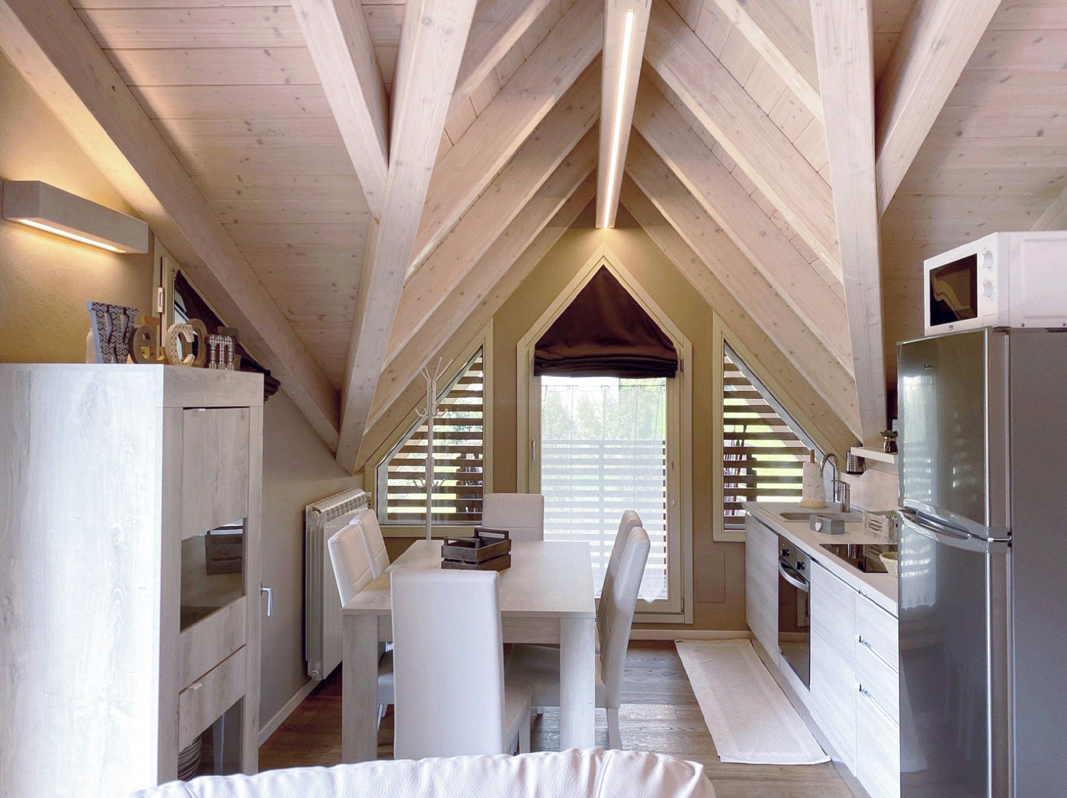 A compact attic bedroom with a white bed, a small table, and a kitchenette.