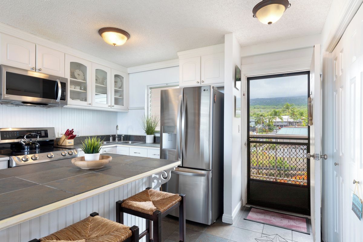 A modern kitchen with a central island, stainless steel appliances, and a view through a door.