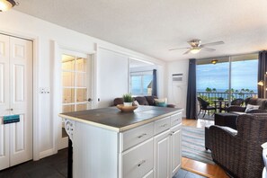 A room with a kitchenette, a dining area with a table and chairs, a sofa, and a view of the ocean. - Kailua Village#609 High Floor, Heart of Downtown, Walk to everything (Kailua Kona)