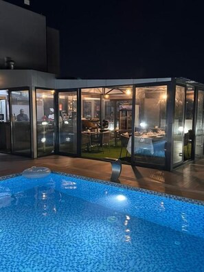 Piscina interna moderna com paredes de vidro, área de estar e espaço para refeições.