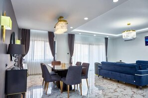 Uma sala de estar moderna com área de jantar, apresentando um sofá azul, um lustre e piso de mármore.