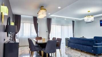Un salon moderne avec un coin repas, comprenant un canapé bleu, un lustre et un sol en marbre.
