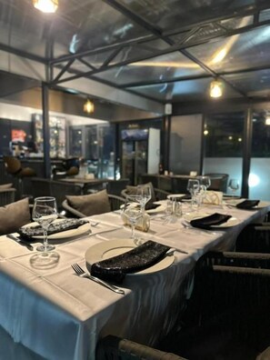 Um restaurante com uma mesa comprida posta para refeição, incluindo pratos, talheres e copos.