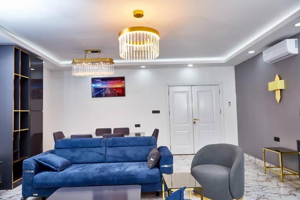 Una sala de estar moderna con un sofá azul, un sillón gris, una araña y un cuadro en la pared.