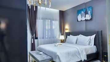 A modern hotel room with a bed, a bedside table, a bench, a painting, and a lamp.