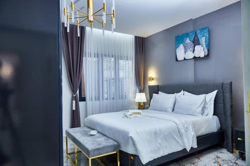 Une chambre d’hôtel moderne comprenant un lit, une table de chevet, un banc, un tableau et une lampe.