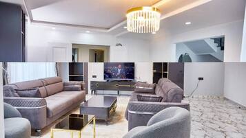 A modern living room with a large flat-screen TV, two sofas, a coffee table, and a chandelier.