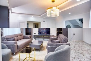 A modern living room with a large flat-screen TV, two sofas, a coffee table, and a chandelier.