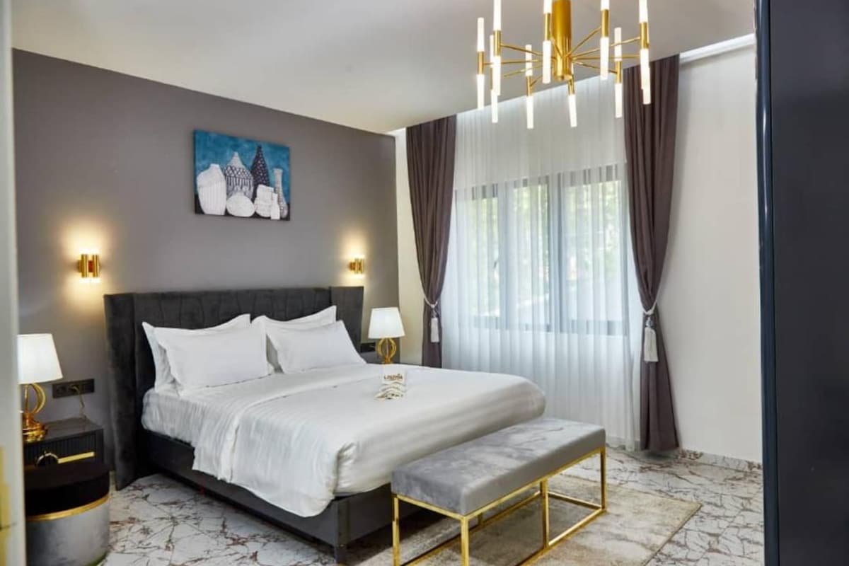 A modern hotel room with a large bed, bedside lamps, a bench, and a painting on the wall.