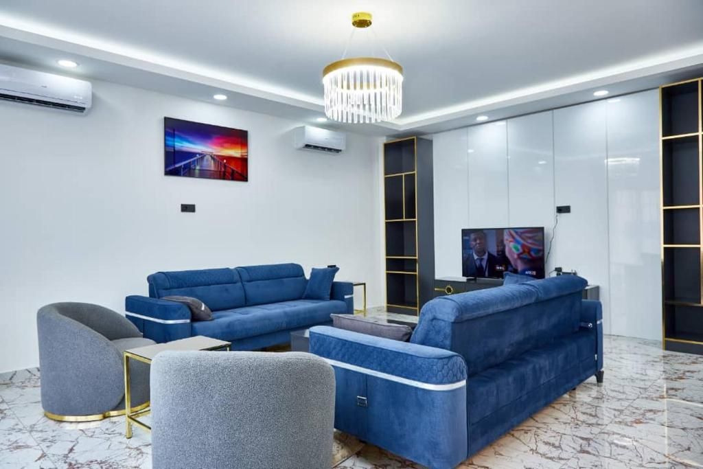 Een moderne woonkamer met een blauwe zithoek, een grijze fauteuil, een klein tafeltje en een televisie.