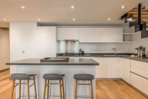 A modern kitchen with a central island, bar stools, and a staircase. - L'Abura - Les Gets - Village Center (Les Gets)