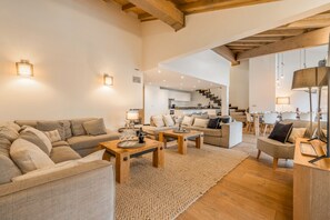 A spacious living area with a sofa, coffee table, and a dining table. There is a staircase leading to an upper level. - L'Abura - Les Gets - Village Center (Les Gets)
