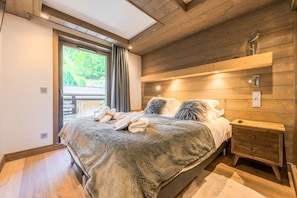 Ein Schlafzimmer mit Holzboden, einem Bett mit flauschigen Kissen, einem Nachttisch und einem Fenster mit Vorhängen.