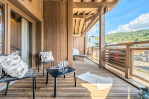 A wooden deck with outdoor furniture, a table with wine glasses, and a view of a mountainous landscape. - L'Abura - Les Gets - Village Center (Les Gets)
