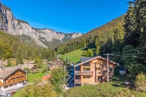 Un refugio de montaña con fachada de madera, un balcón y vistas del bosque y montañas circundantes.