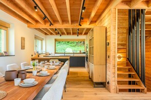 Una cocina moderna con vigas de madera, un comedor con una mesa larga y vistas a la vegetación.