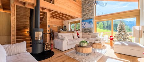Un salón amplio con una chimenea grande, vigas de madera y vistas al exterior.