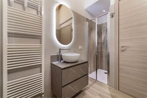 A modern bathroom with a white sink, marble vanity, a glass shower enclosure, and a wooden door. - AffittiPontediLegno-Sofia&Ferdy Alpine LuxuryView (Ponte di legno)
