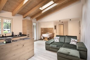 A modern kitchen with wooden cabinetry and a dining area with a green sofa and table. - AffittiPontediLegno-Sofia&Ferdy Alpine LuxuryView (Ponte di legno)