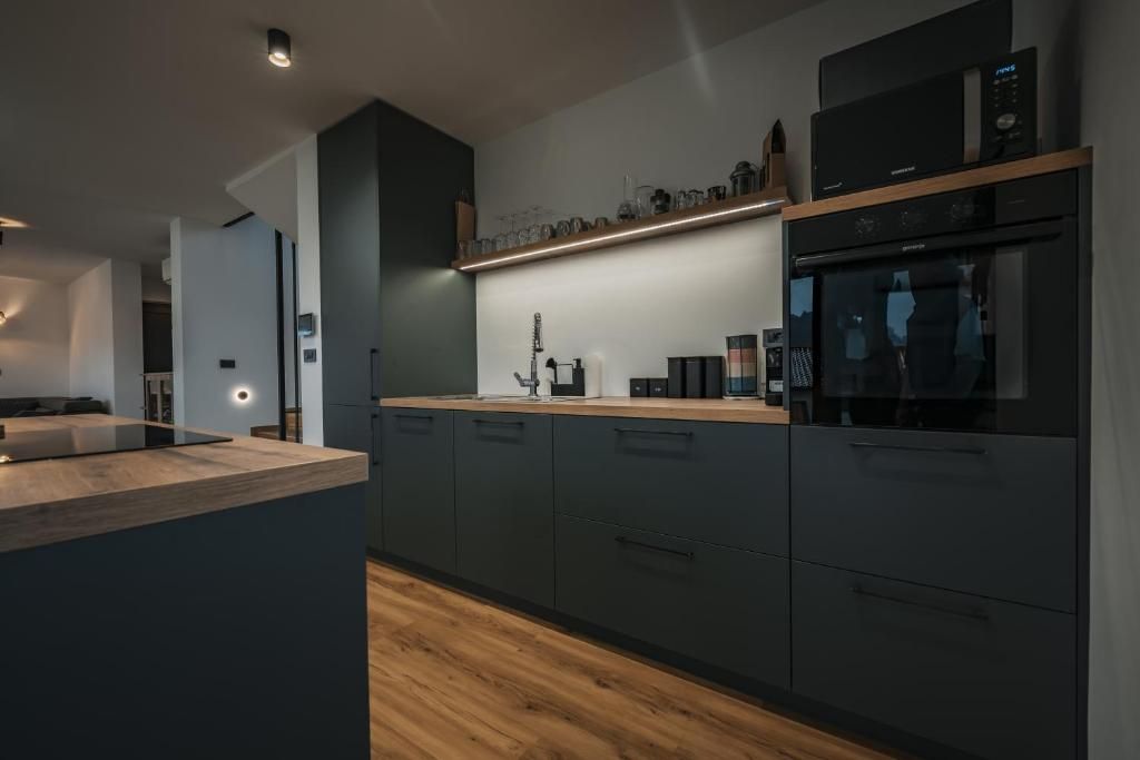 Una cocina moderna con muebles oscuros, encimera de madera y electrodomésticos integrados, incluyendo un microondas y horno.