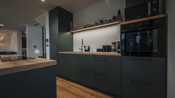 Una cocina moderna con muebles oscuros, encimera de madera y electrodomésticos integrados, incluyendo un microondas y horno.