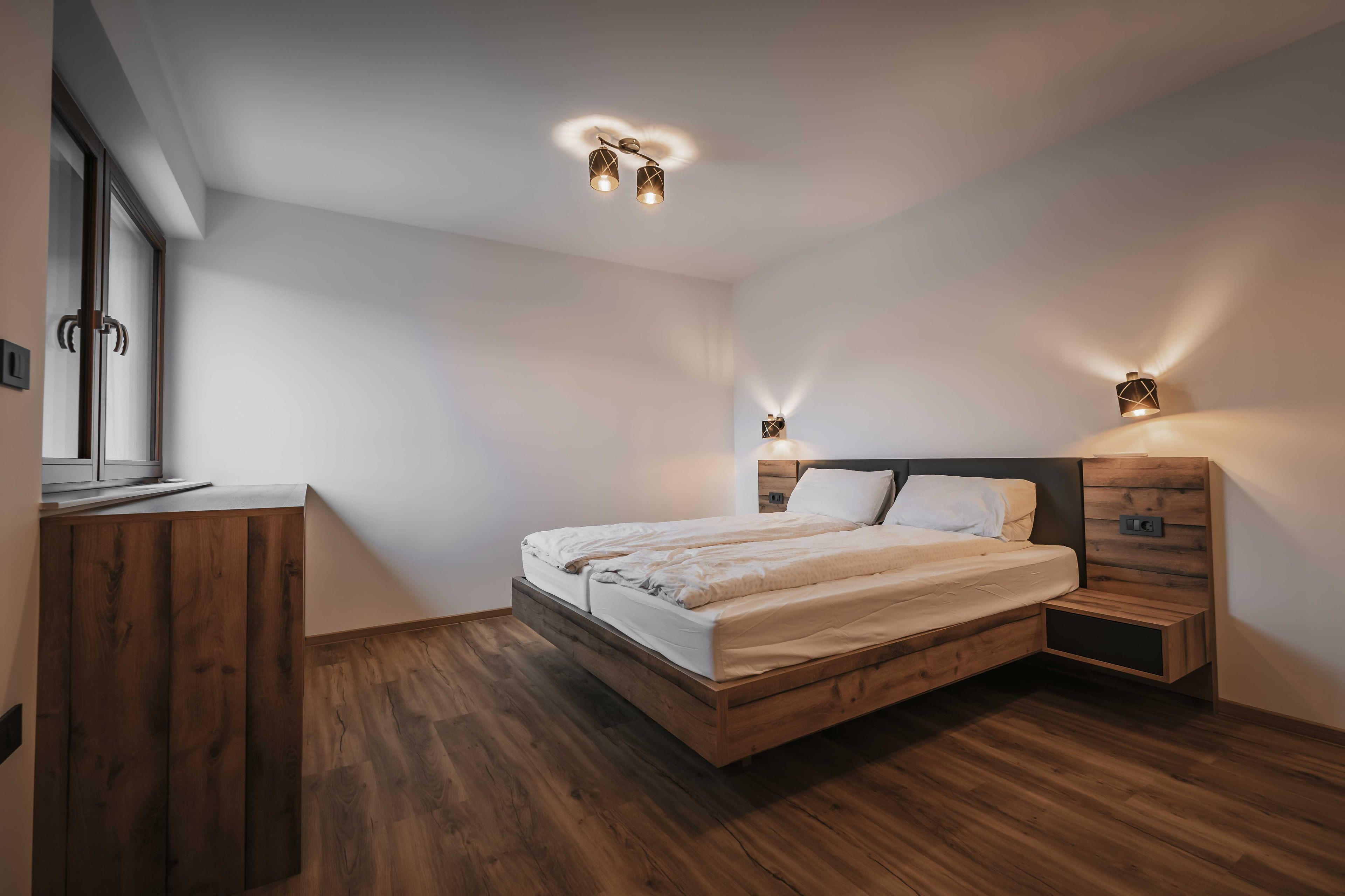 Un dormitorio moderno con una cama de madera, mesitas de noche y un armario.